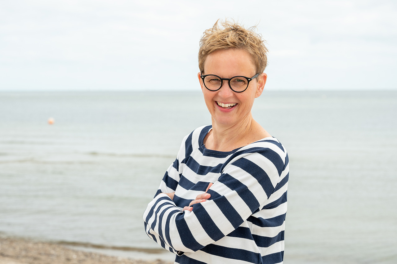 Ayurveda-Coaching in Kiel Symbolisch für Ayurveda: Marlene Rostig im blau-weiß geringelten Pullover am Ostsee-Strand in Kiel