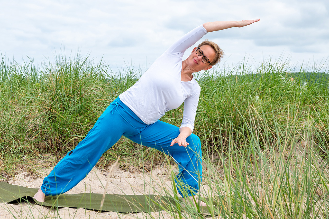 Yoga-Kurse in Kiel Marlene Rostig auf grüner Yogamatte praktiziert die Yogaübung „gestreckter seitlicher Winkel” in der Dünenlandschaft in Kiel